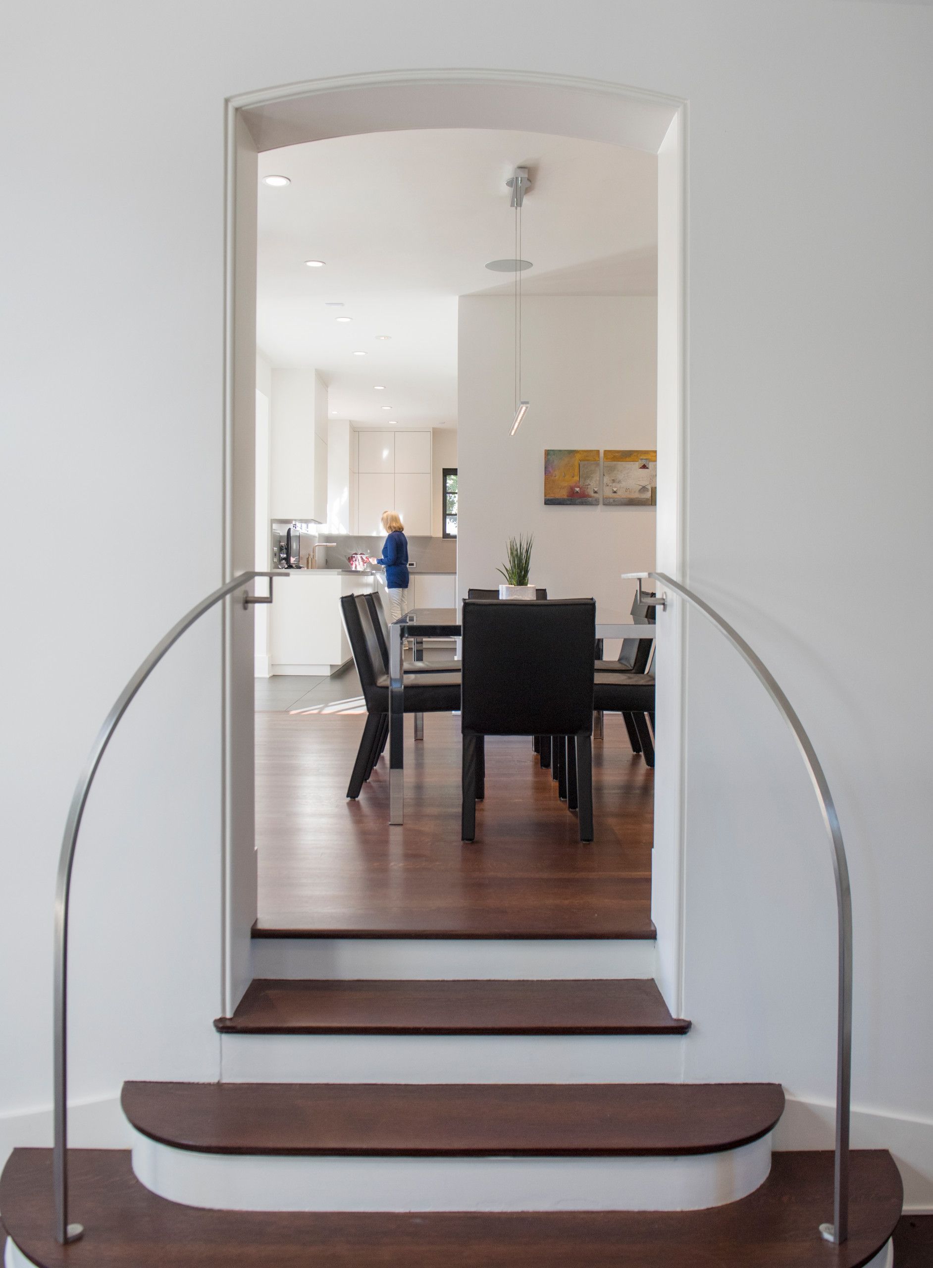 Arched doorway with steps leading into dining room. Dark wood steps, dark table and chairs, light walls.