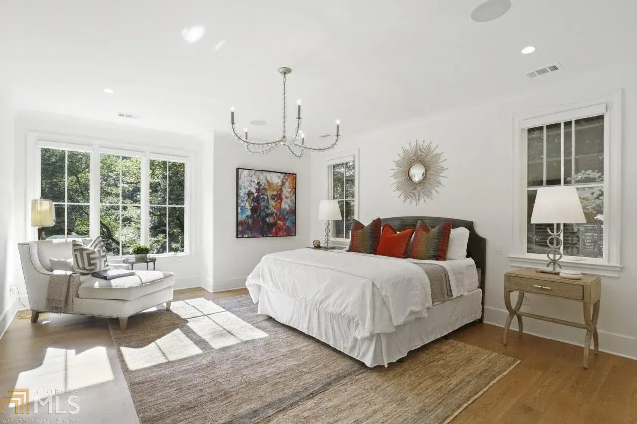 Spacious, bright bedroom with white walls, large windows, and a king bed. Sunlight streams in, illuminating the neutral tones.