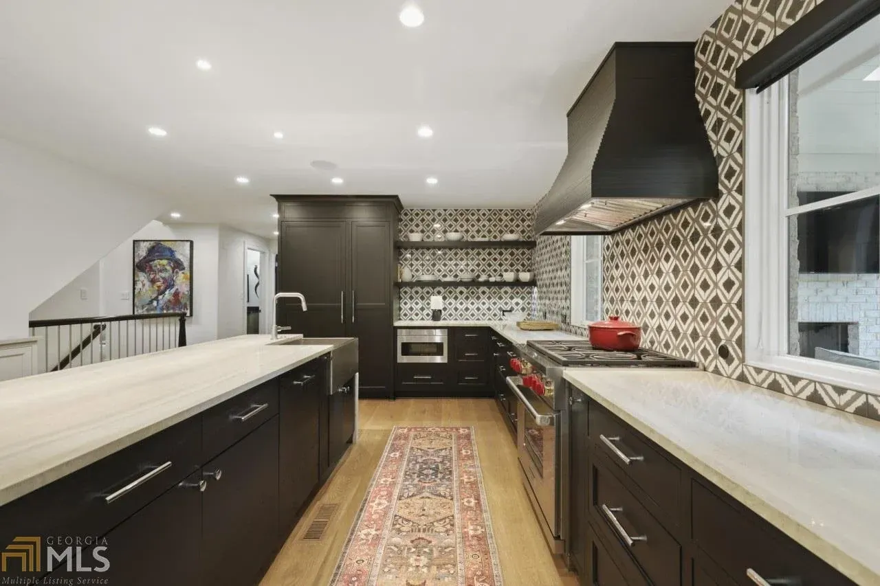 Modern kitchen with dark cabinets, light countertops, and patterned backsplash.