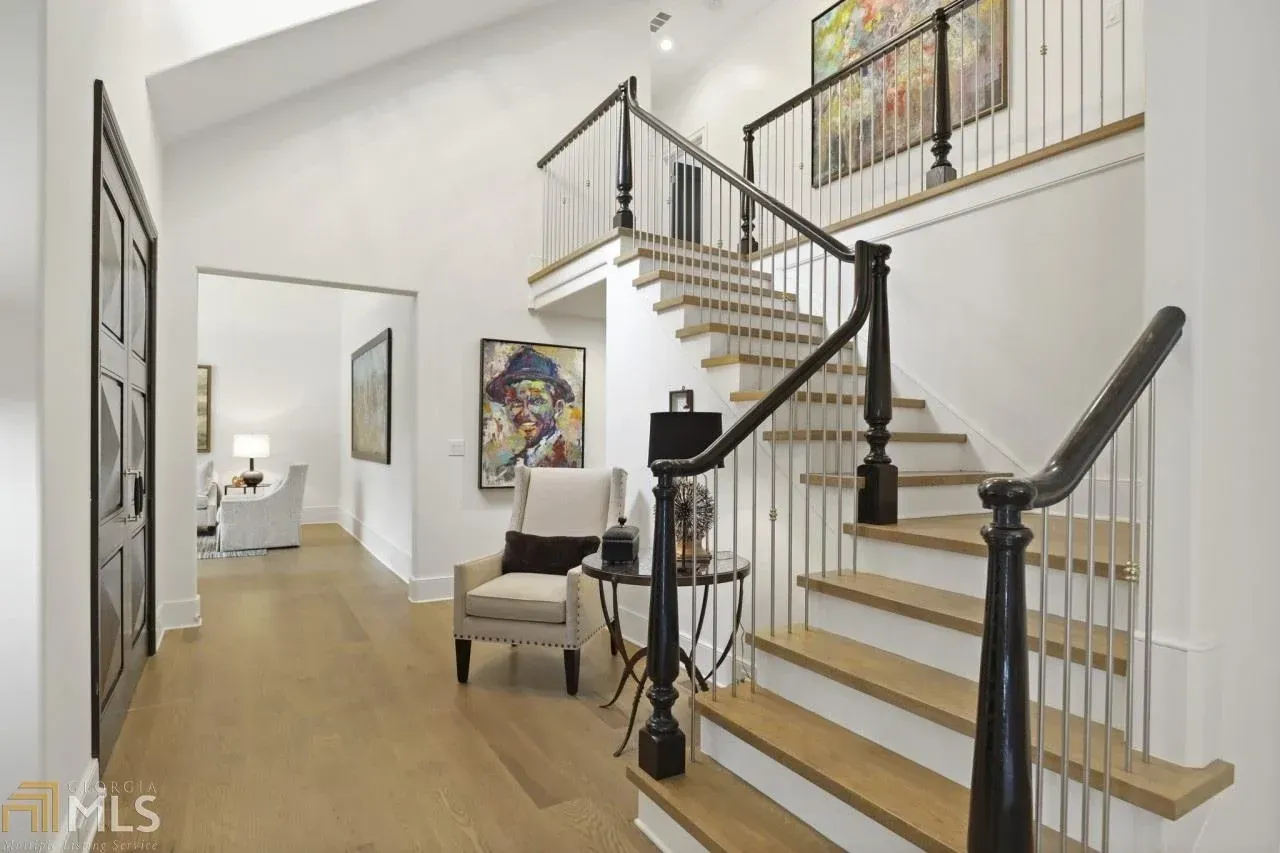Entryway with staircase, light wood floors, and white walls, featuring art and a seating area.