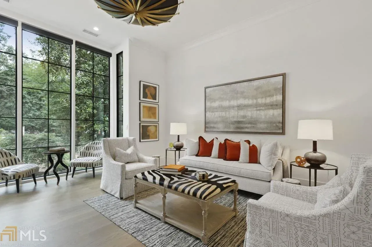 Living room with white walls, large windows, and modern furniture in neutral tones with orange accents.