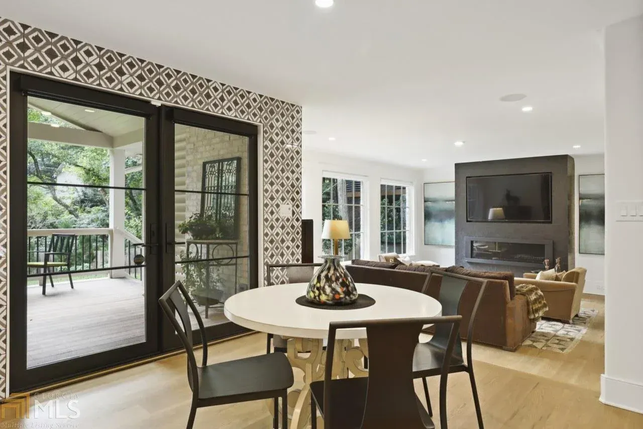 Dining room with a round table, chairs, patterned wall, and doors leading to a porch.