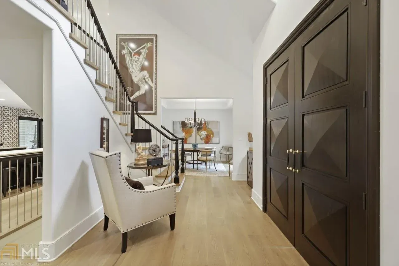 Entryway with staircase, chair, artwork, and dark double doors, light wood floors.