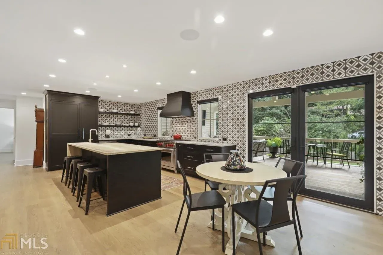 Spacious kitchen with black cabinets, patterned wall, and a dining table with an outdoor view.
