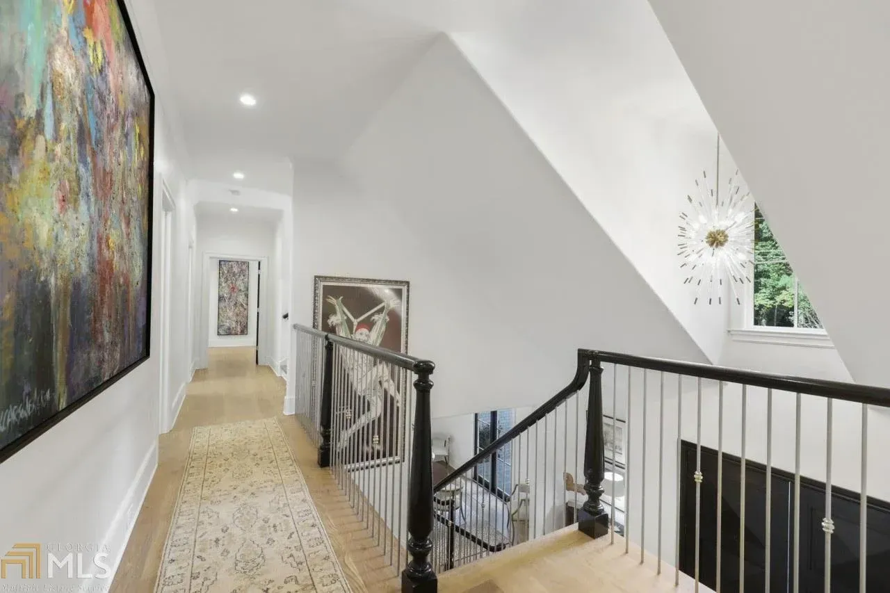 Hallway with artwork, light wood floors, and black and silver railing.