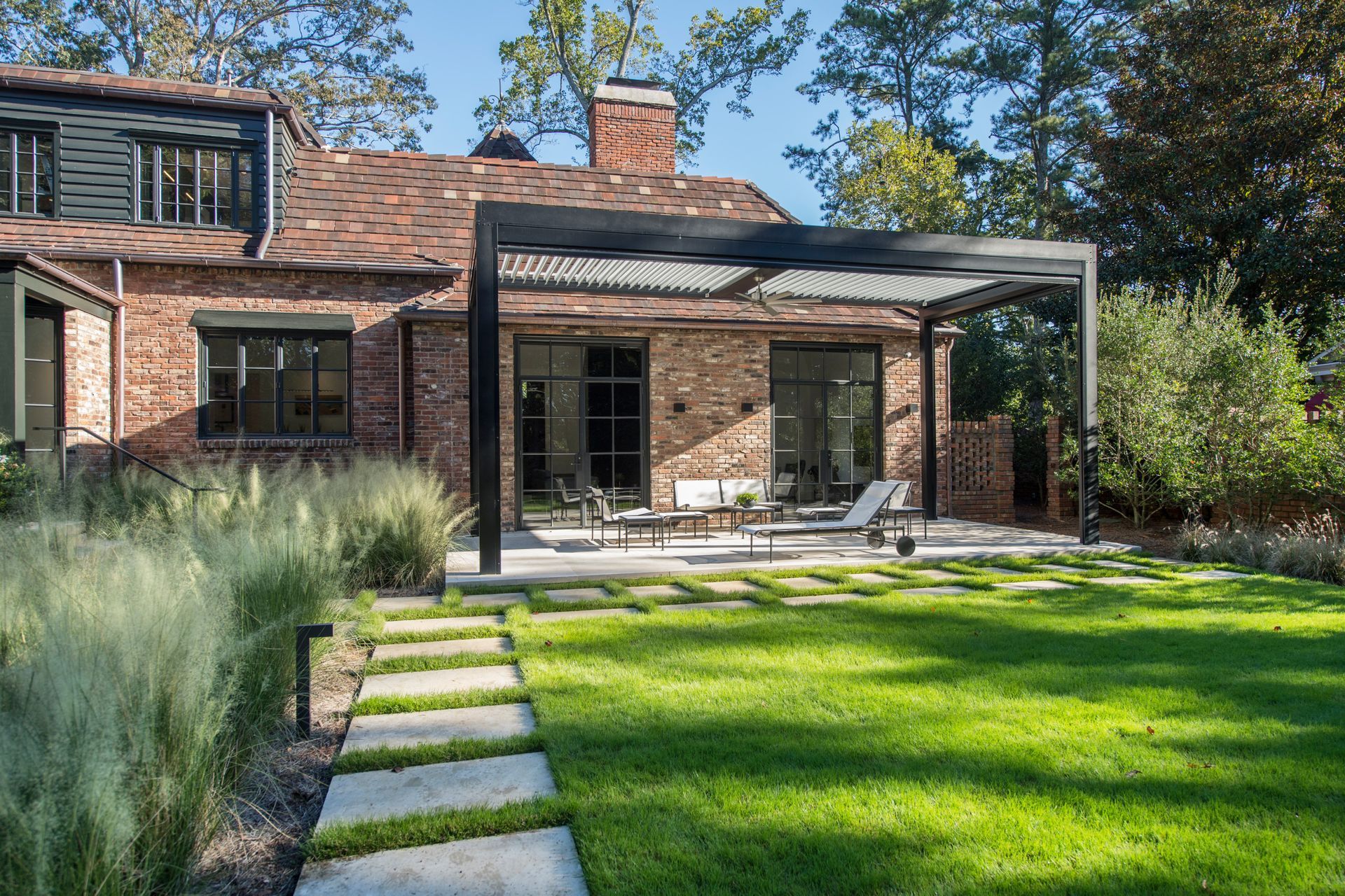 Brick house with pergola over patio, grass, stone walkway, and landscaping.