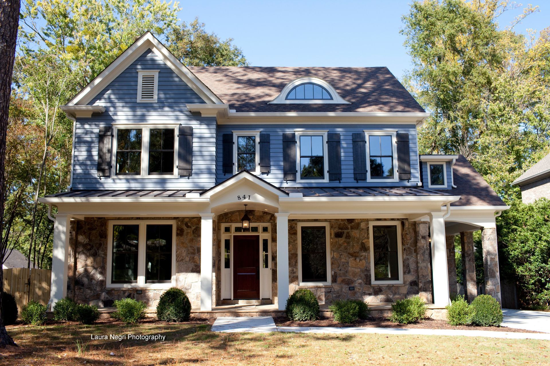 Two-story blue house with stone accents, front porch, and brown roof.