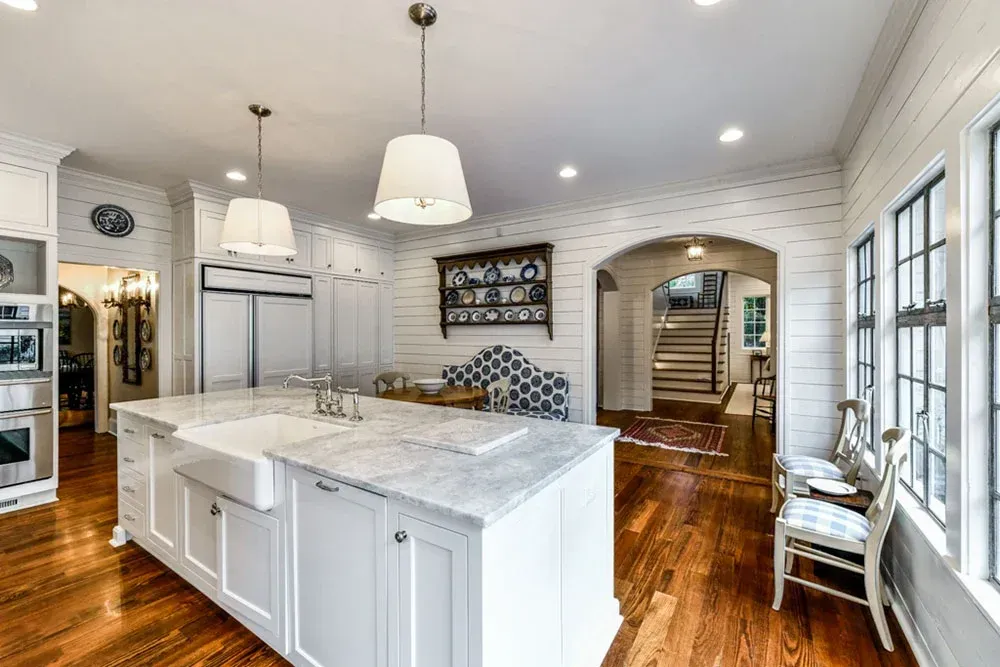 White kitchen with large island, white cabinets, wood floors, and arched doorway.