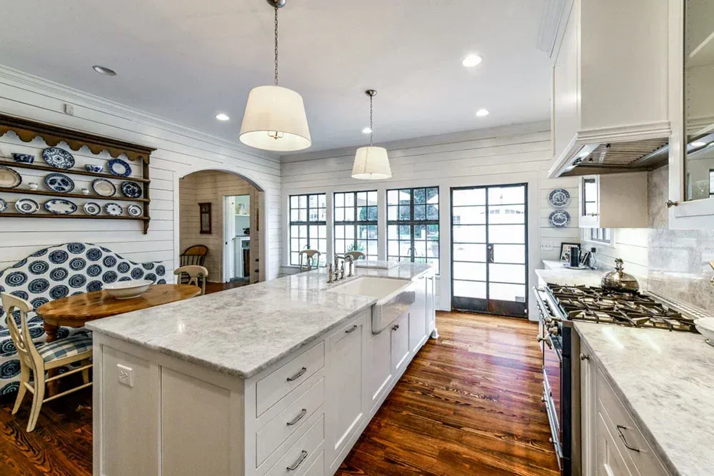 White kitchen with island, wood floor, blue and white patterned seating, and glass doors.