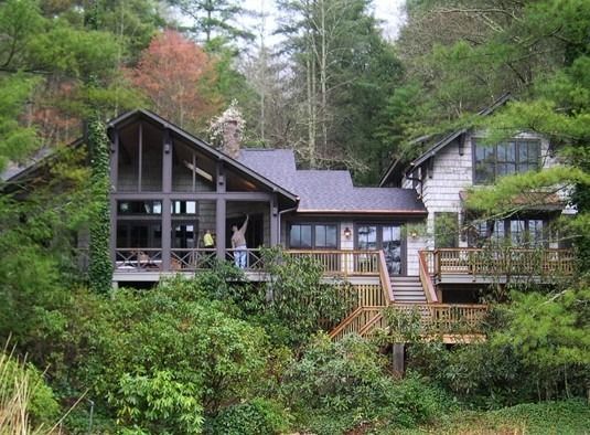 A house in a forest with a wooden deck and a person on the porch.
