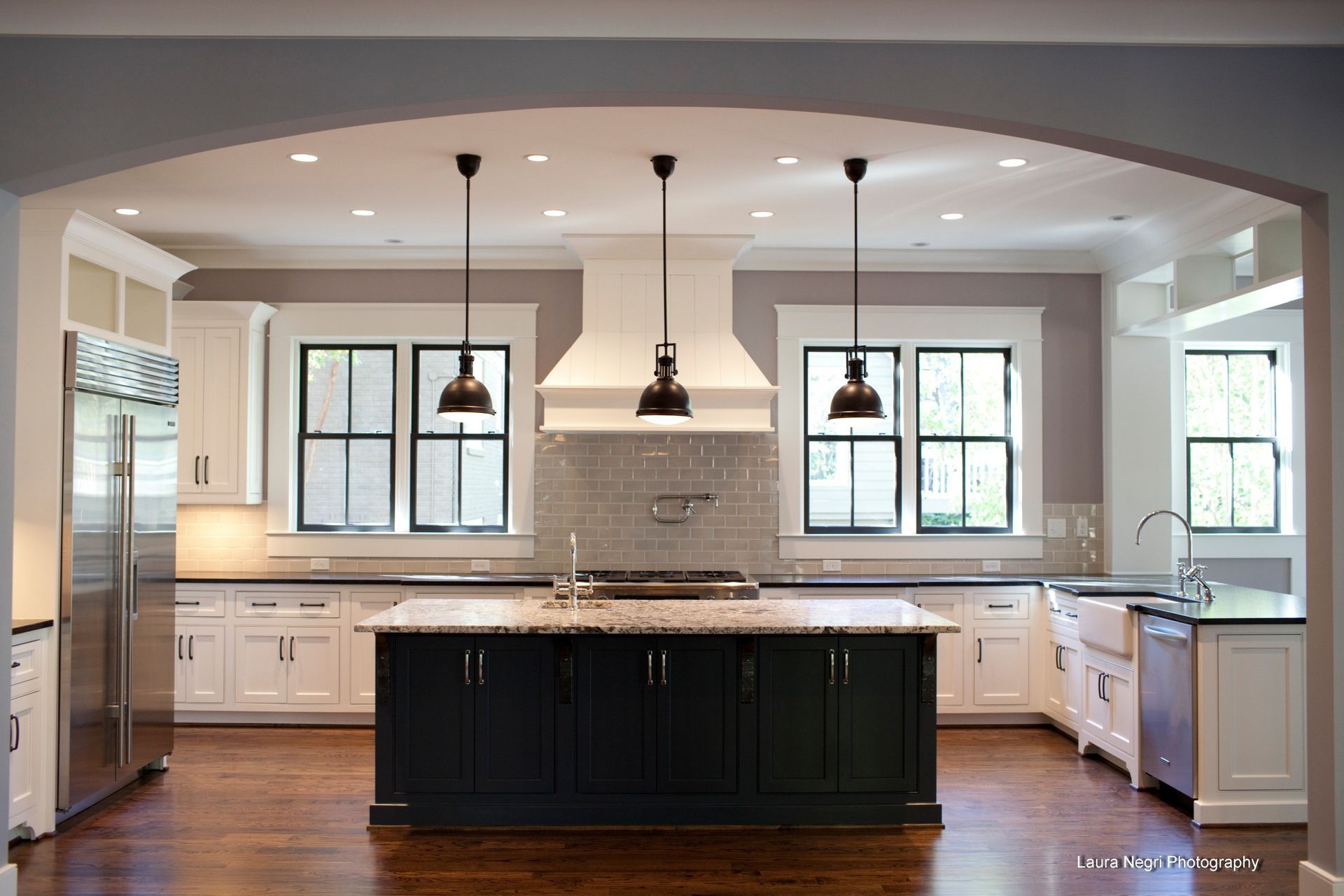 Spacious kitchen with dark island, white cabinets, stainless steel appliances, and three pendant lights.