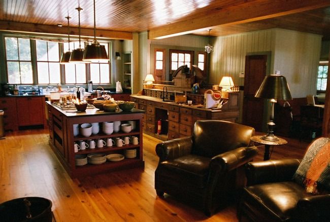 Rustic kitchen and living area with wooden floors, island, dark leather armchairs, and natural light.
