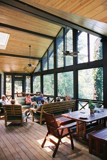 Screened porch with people sitting on wood furniture, large windows, and a wooden ceiling.