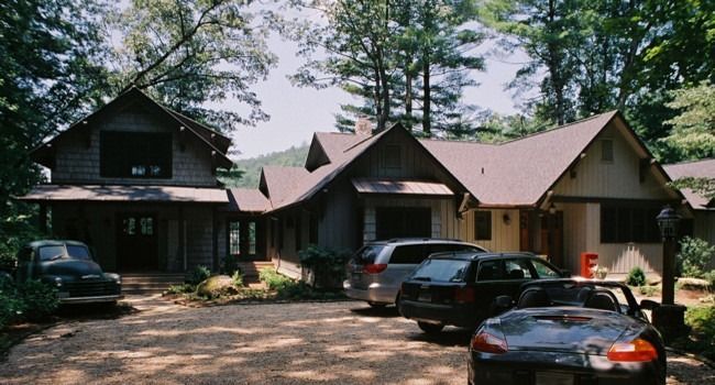 Houses with a gravel driveway, cars parked in front. The buildings are nestled among trees, and the sky is visible.