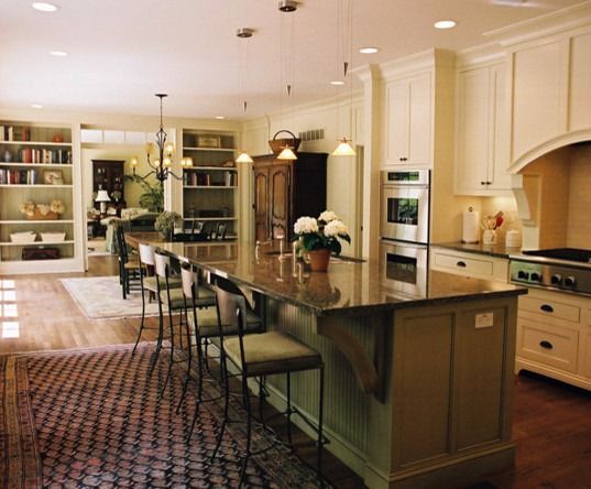 Kitchen with large island, seating, cabinets, built-in appliances, and bookshelves.  Warm tones, rug, natural light.