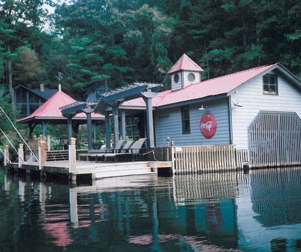 Boathouse with red roof and open-air deck on a lake, with surrounding trees.