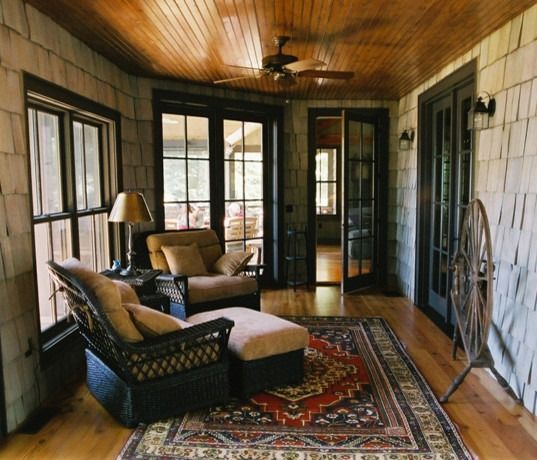 Sunroom with wooden ceiling and walls, wicker furniture, antique rug, and French doors.