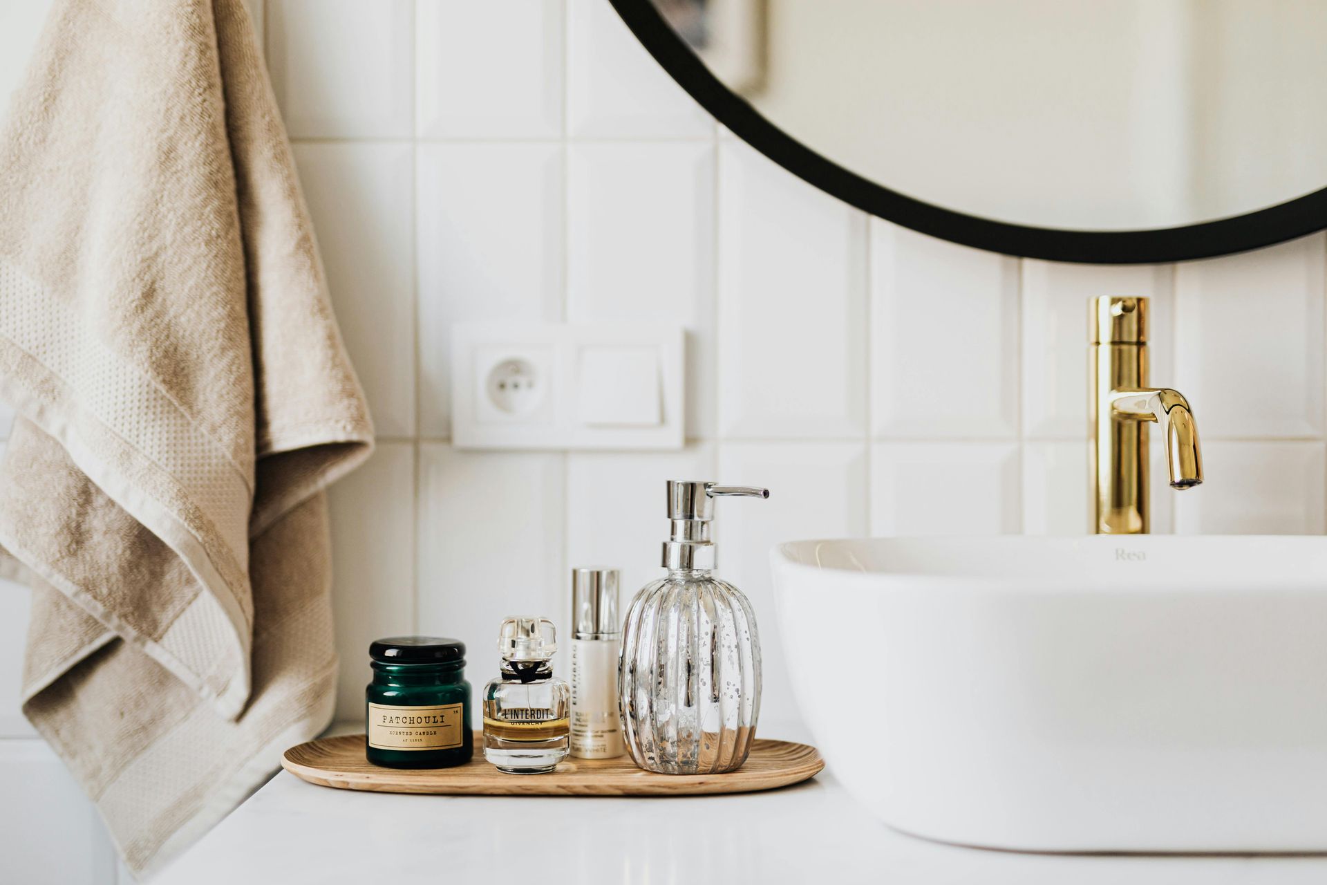 A bathroom with a sink , mirror , towel and bottles of perfume.