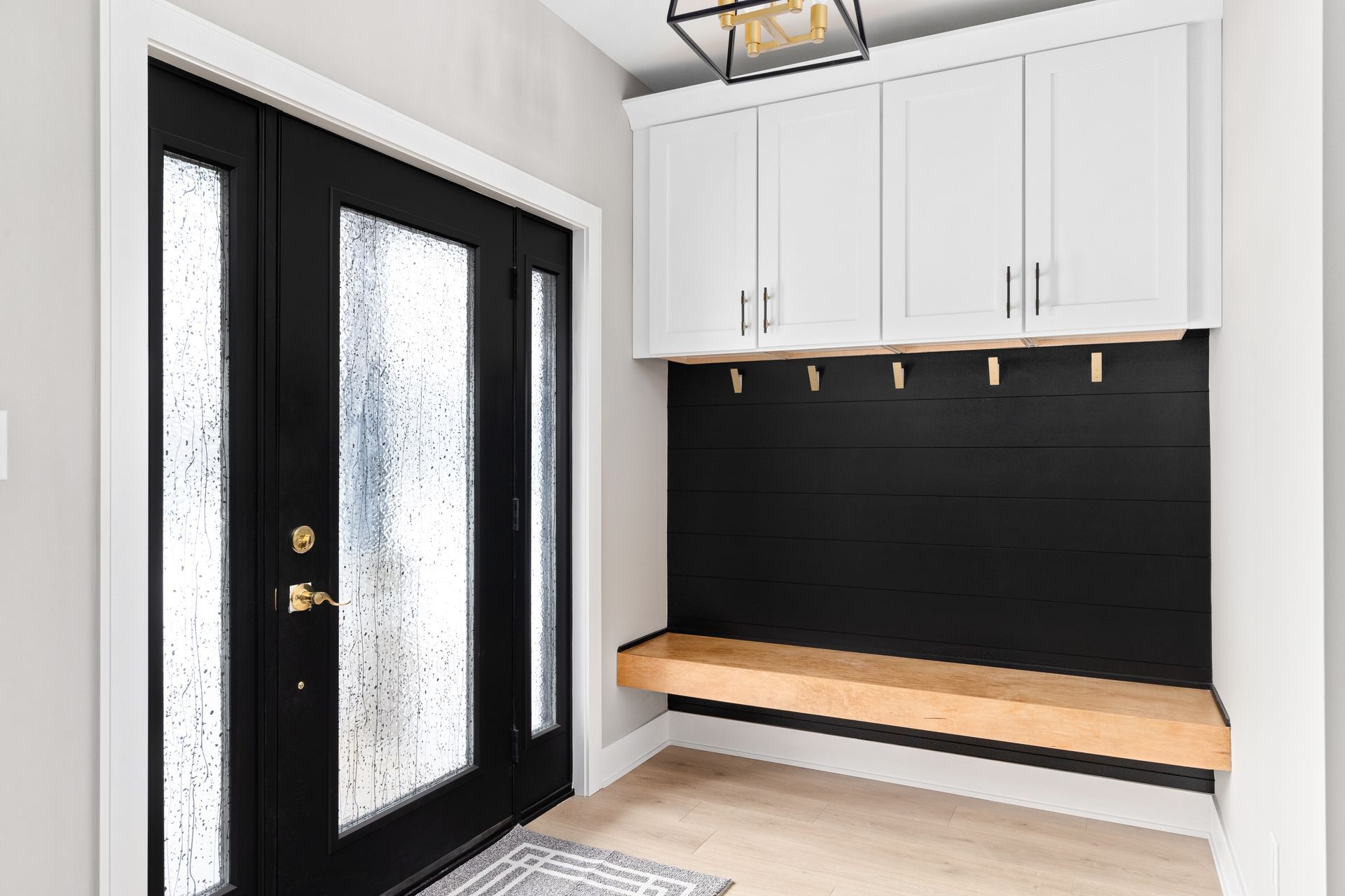 A hallway with a black door , white cabinets , and a wooden bench.