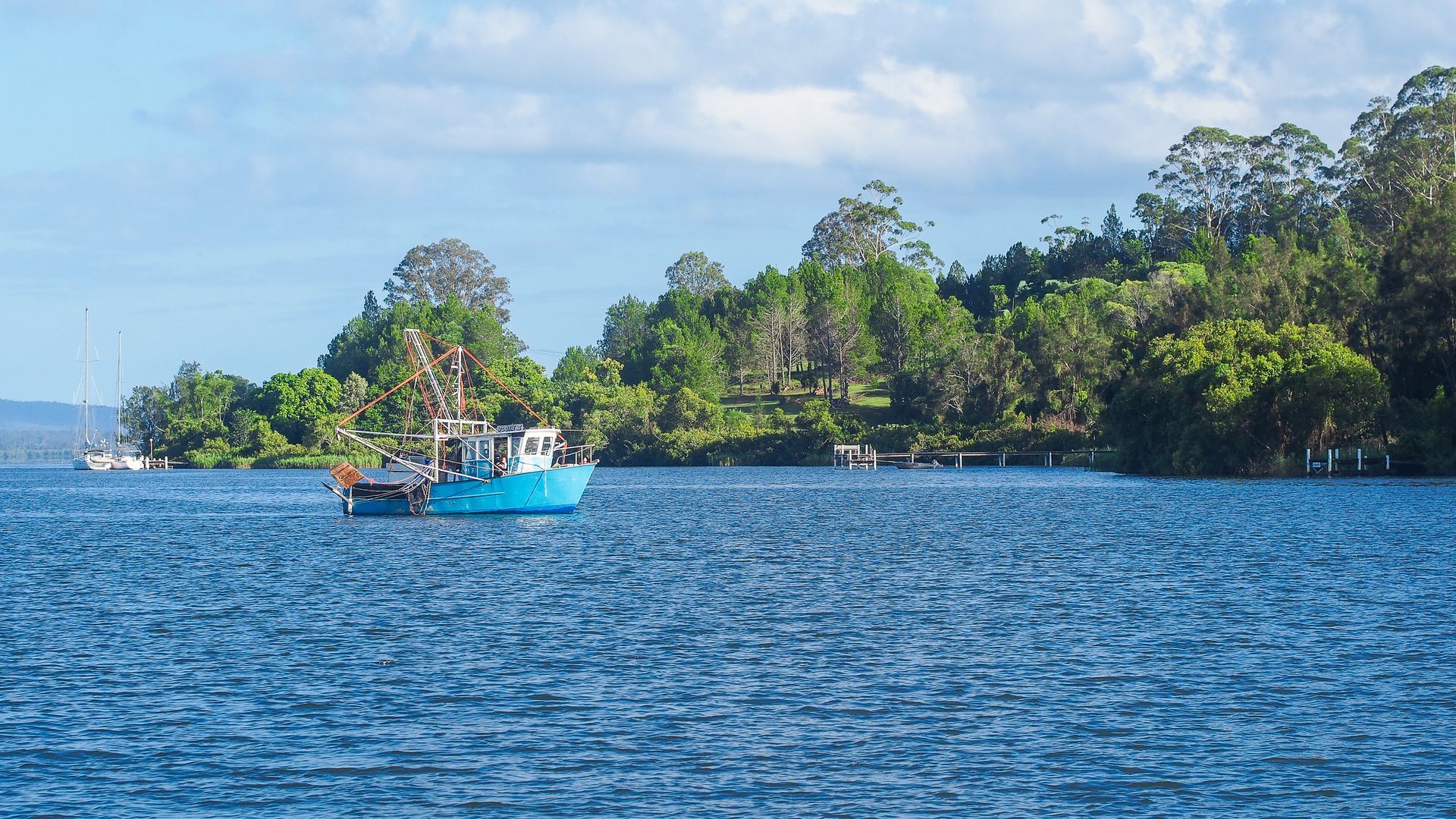 Blue Boat on a Blue Body of Water, Trees Line the Shore Under a Blue Sky — Pootanky Maclean, NSW