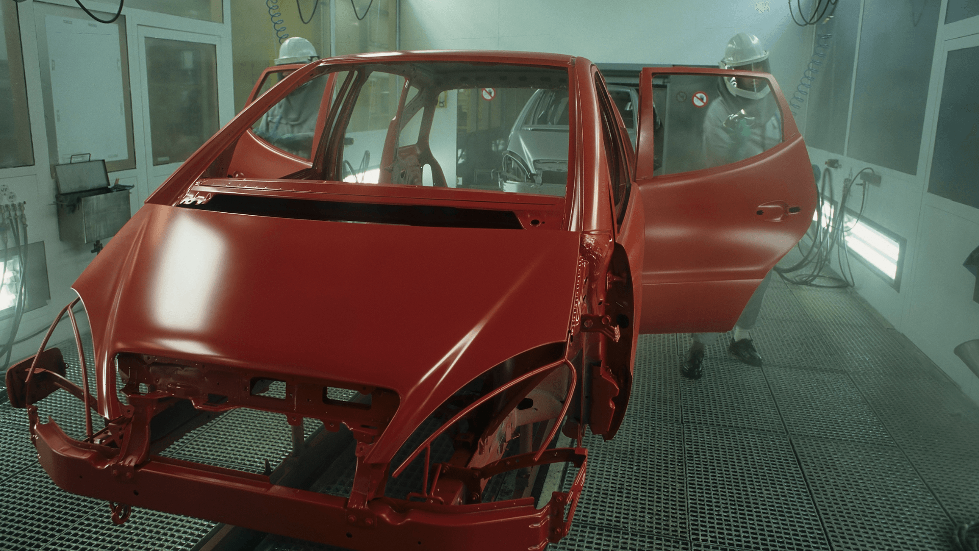 A red car is being painted in a paint booth.