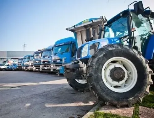 Un trattore blu è parcheggiato accanto a una fila di camion blu