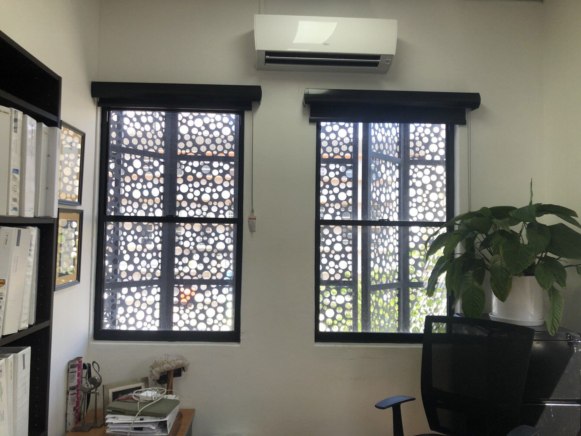 Two windows with decorative screens and black frames in a room, with an AC unit above.