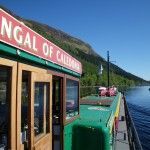 Boat on Loch Lomond with mountain backdrop. Sign on the boat reads 