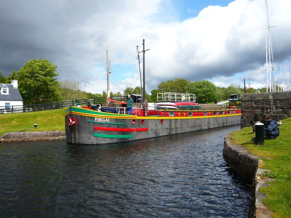 Colorful barge in a canal lock with cloudy sky overhead and grassy banks.