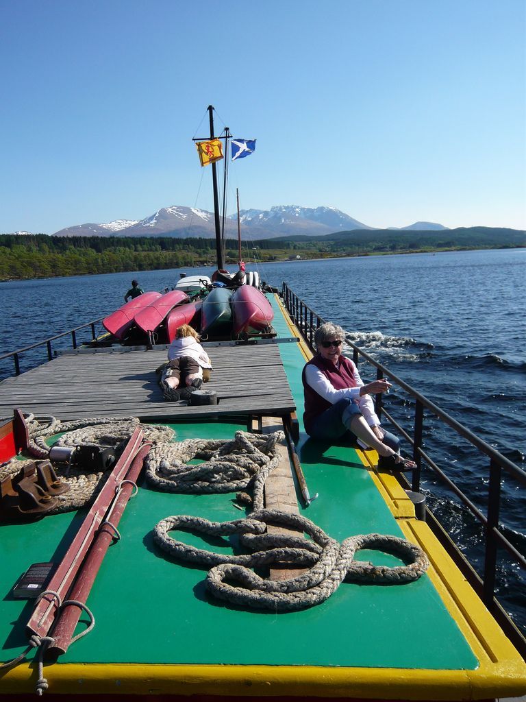 Person on a boat dock with mountains in the background. Boats are visible.