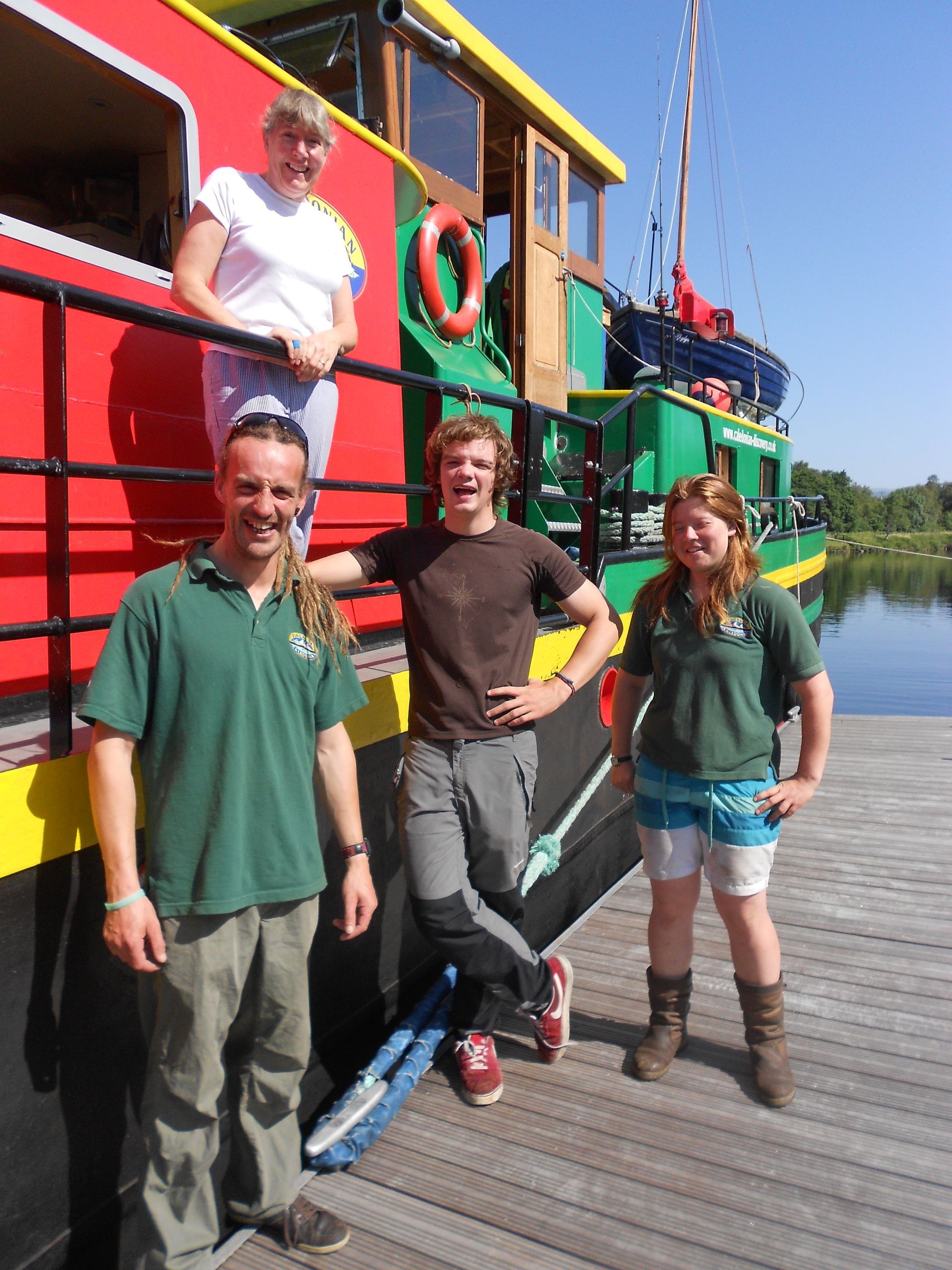 Four people stand near a brightly colored boat at a dock.
