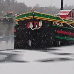 A black boat named Fingal with green and red accents, in a snowy harbor.