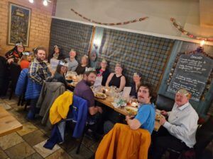 People at a restaurant table, many wearing paper crowns. Restaurant interior, food on table.