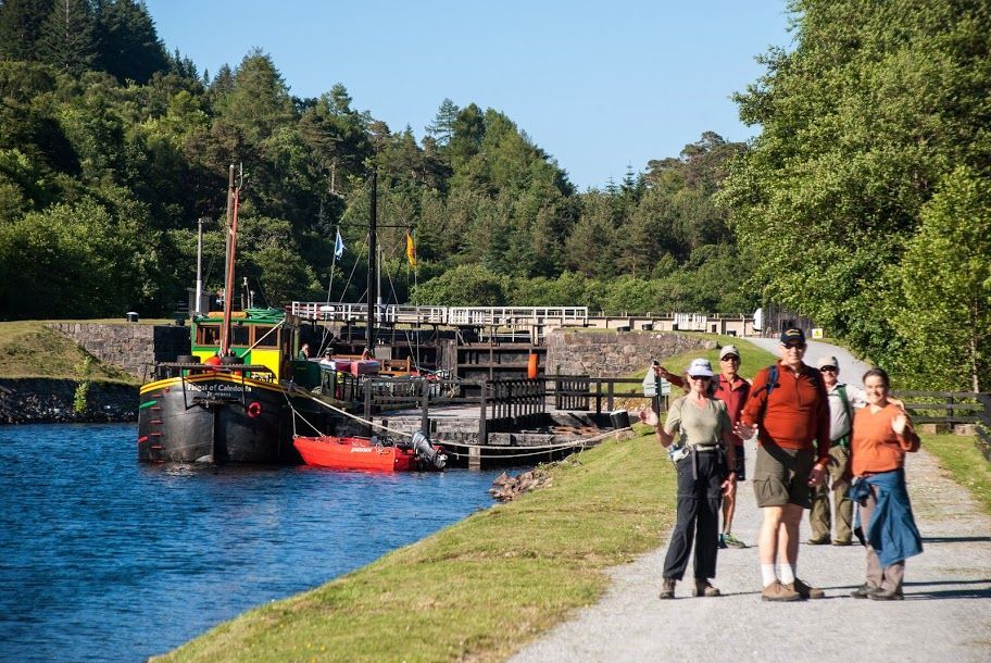 Group of people walking by a canal with a boat and lock on a sunny day.