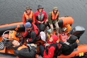 People wearing life vests in an orange inflatable boat on water.