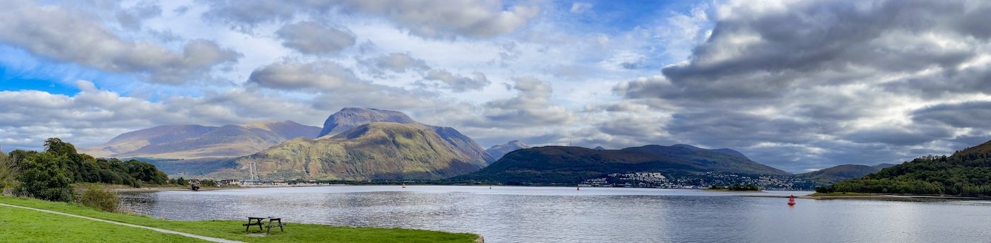 A lake surrounded by mountains and a cloudy sky. The water is calm, and the hills are lush green.
