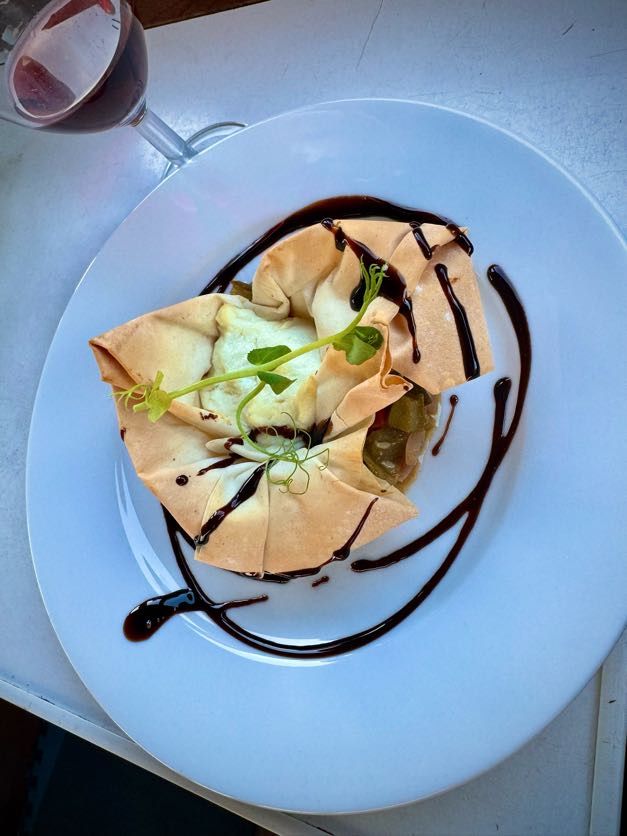 A filo pastry-wrapped appetizer drizzled with balsamic glaze, garnished with greens, on a white plate.