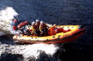 Orange RNLI rescue boat speeding through water, with several people aboard.