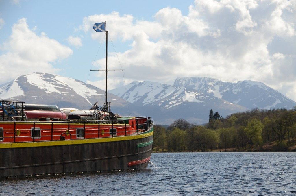 Boat with Scottish flag on water, mountains in the background, sunny day.
