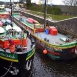 Two canal boats in a lock, green, black, and red paint, with kayaks on one.