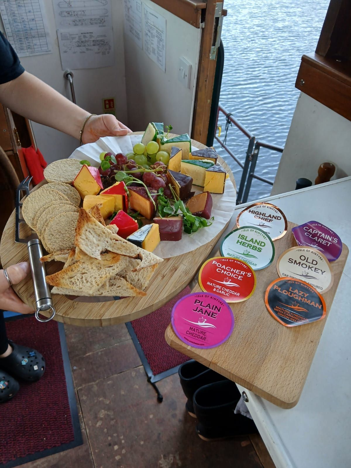 A person holding a charcuterie board with cheese, crackers, grapes, and meat on a boat.