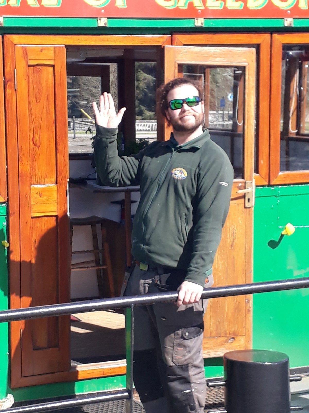 Man waving, standing by green and brown boat cabin with open doors.