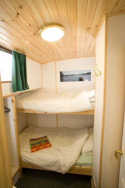 Bunk beds in a small cabin. Wooden ceiling and walls, white bedding, green curtain, artwork on wall.