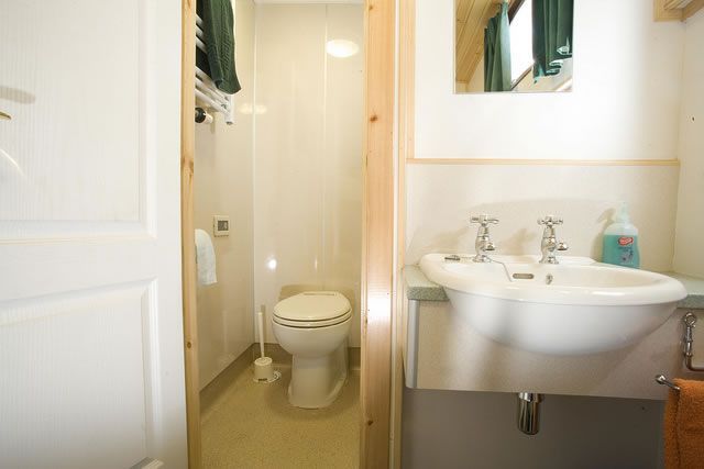 Small bathroom with a toilet, sink, and mirror. White walls, wooden door frame, and towel rack.