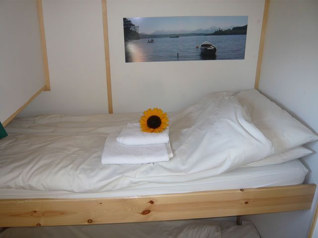 Cozy, narrow bunk bed with white linens and sunflower. Photograph of water above.