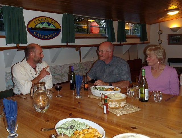 Three people seated around a wooden table indoors, eating and talking. A California sign is visible on the wall.