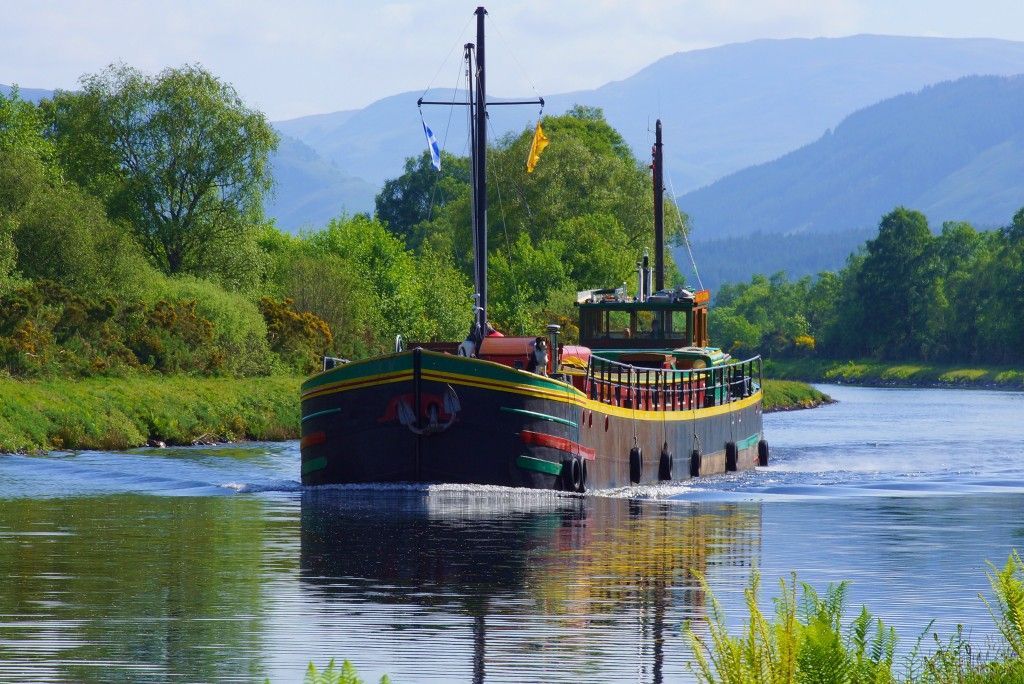 Boat sailing on a river, trees and mountains in the background.