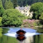 Boat on lake with castle in background. Lush trees and foliage with blue sky.