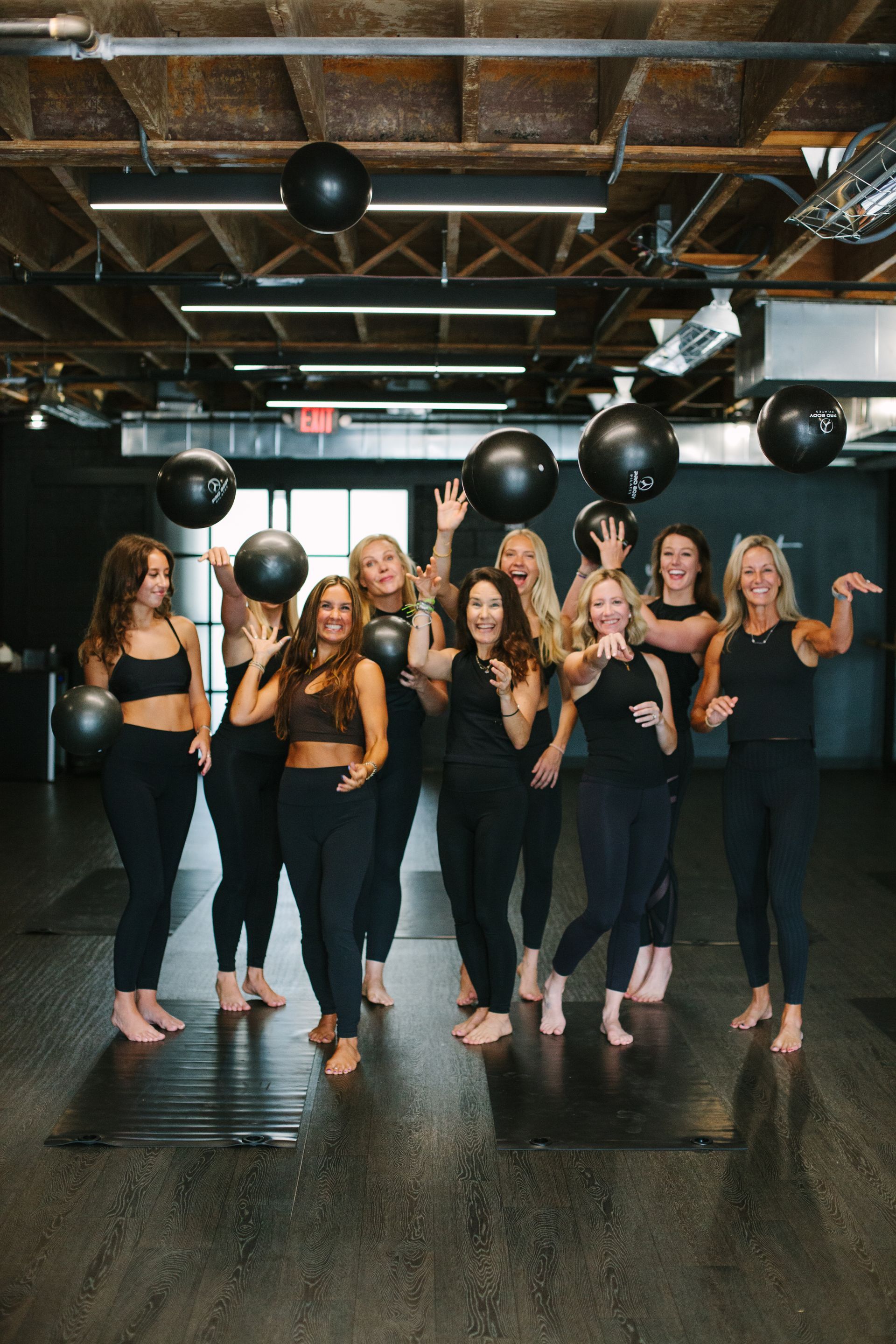 Group of women celebrating in a studio; wearing black outfits, holding balloons.