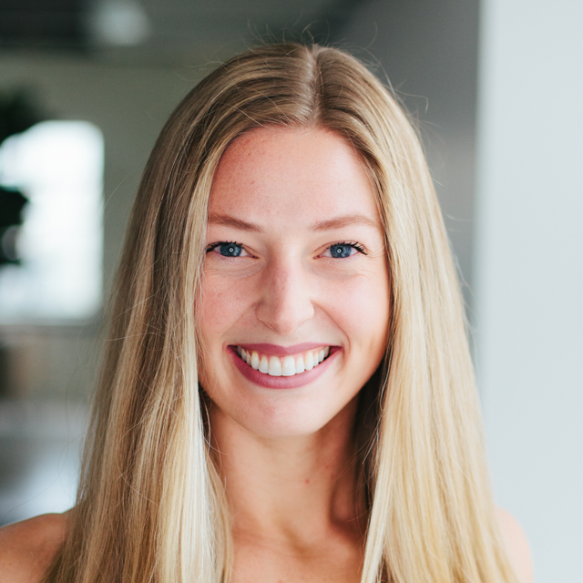 Blonde woman smiling, looking at the camera, in a well-lit, modern space.